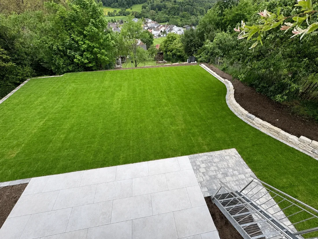 Neu angelegter Garten mit Plattenterrasse, Rollrasen und geschwungener Natursteinmauer mit Blick ins Tal